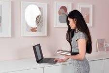 A businesswoman stands indoors, using a laptop, reflecting focus and professionalism.
