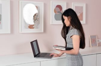 A businesswoman stands indoors, using a laptop, reflecting focus and professionalism.