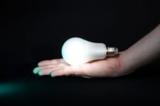 Hand holding an illuminated LED bulb on a dark background, symbolizing energy efficiency and light innovation.