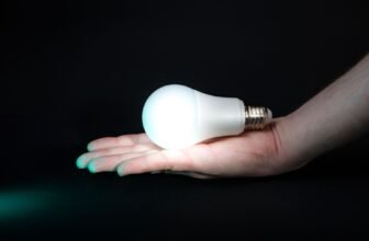 Hand holding an illuminated LED bulb on a dark background, symbolizing energy efficiency and light innovation.