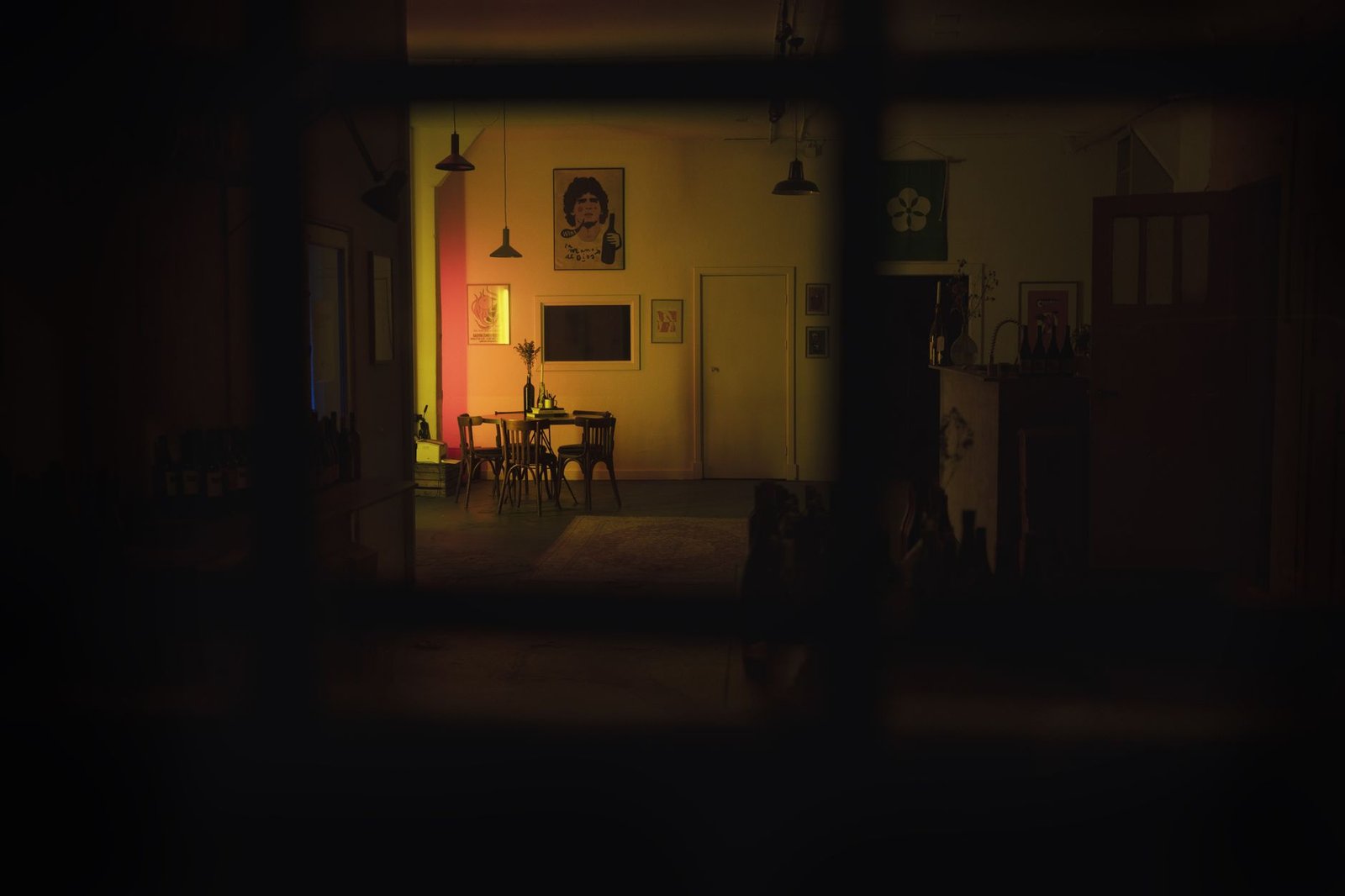 A dimly lit dining room with vintage chairs and table, seen through a window at night.