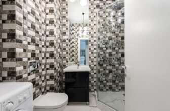 Interior of bright washroom with washing machine near toilet next to shower and sink with tap