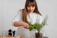 A woman in a white sweater tending to a potted herb plant indoors, showing focus and care.