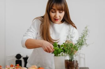 A woman in a white sweater tending to a potted herb plant indoors, showing focus and care.