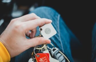 A close-up of a hand holding a set of car keys with various keychains and tags. Indoor setting.