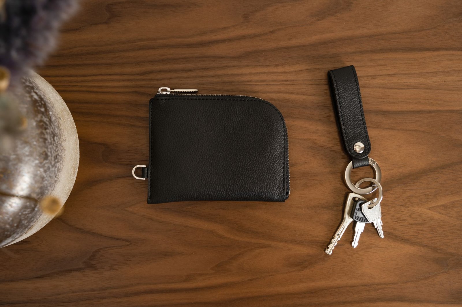 Close-up of a black leather wallet and keychain with keys on a smooth wooden surface.
