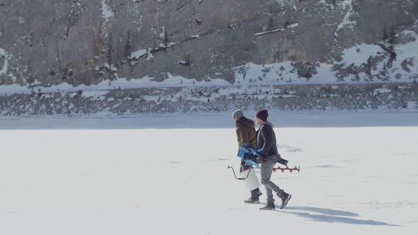 Friends carry ice fishing gear across a frozen alpine lake in the canadian rockies