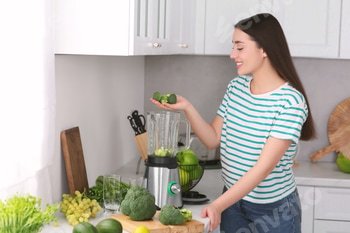 Woman adding broccoli into blender for smoothie in kitchen